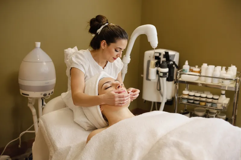 Esthetician brushing a clay mask onto a relaxed client's cheek